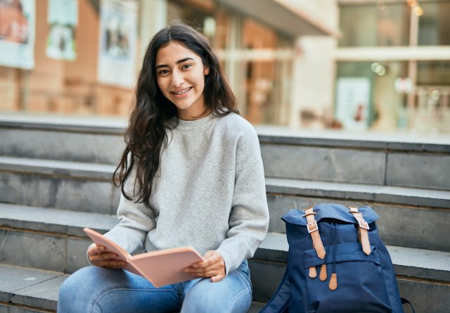 Young student smiling happy reading book at the university.